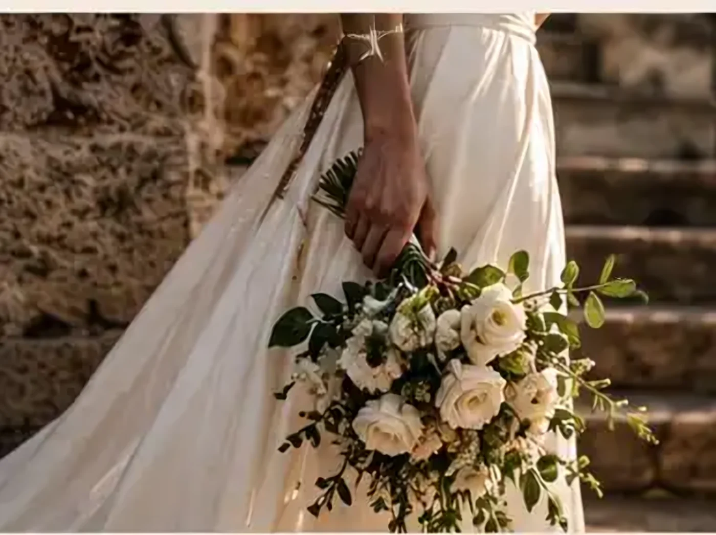 A bride holding a bouquet of white roses on stone steps